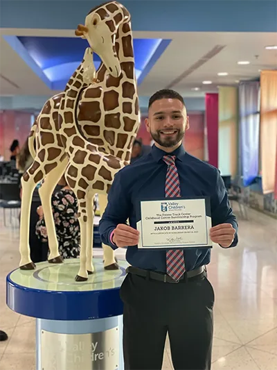 Young man holding a certificate in front of a giraffe statue